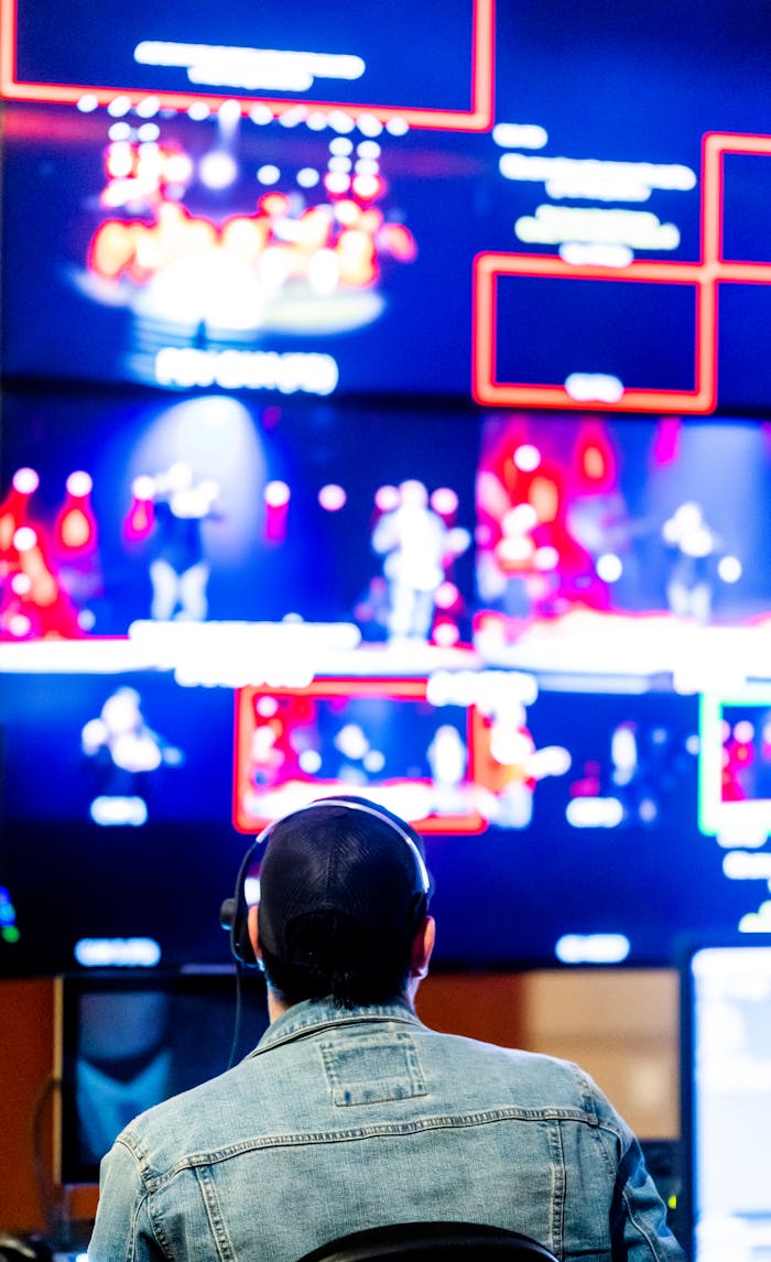 Technician with headphones monitoring live video feeds on multiple screens.